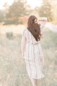 pregnant in field floral dress sun in hair wind blowing in hair looking away